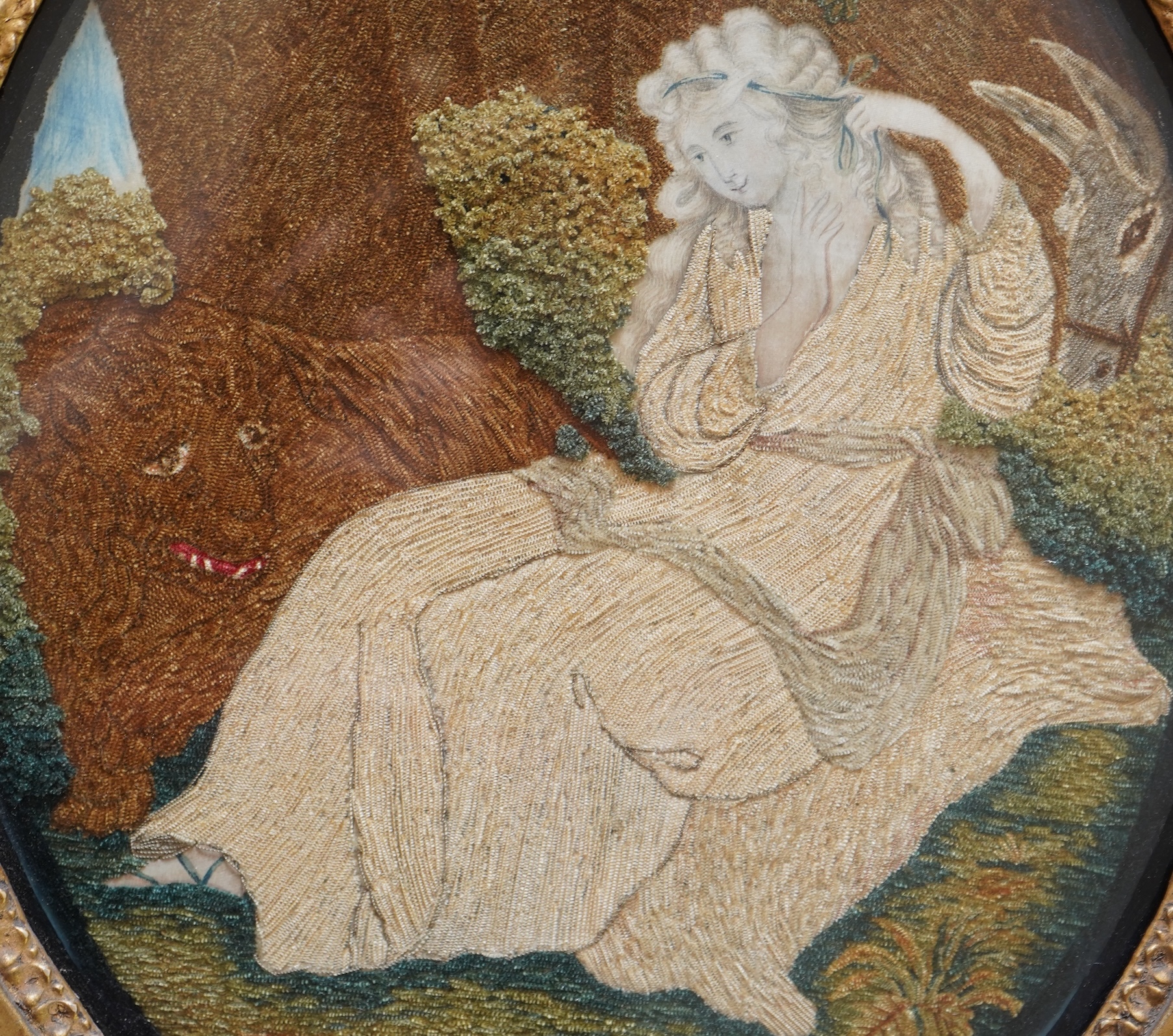 A pair of unusual early 19th century oval silk Chenille embroideries, one depicting a seated lady surrounded by a lion and donkey, the other depicting a seated shepherdess under tree with two sheep. Both have water colou